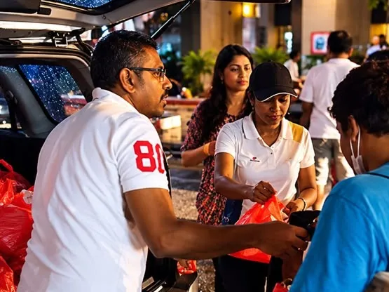 A LIFE Malaysia volunteer hands a bag of food from a car boot to a man on a Kuala Lumpur street at night, 2015