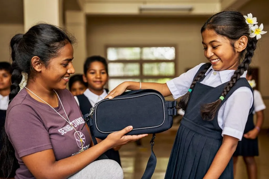 A LIFE Malaysia volunteer hands a new school bag to a smiling Tamil school girl